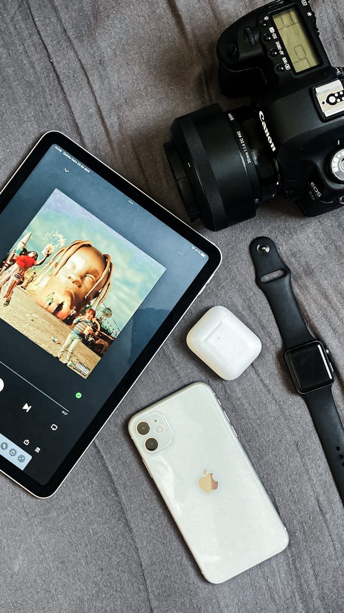 Top view of tablet, camera, smartphone, smart watch, and earbuds on a gray background.
